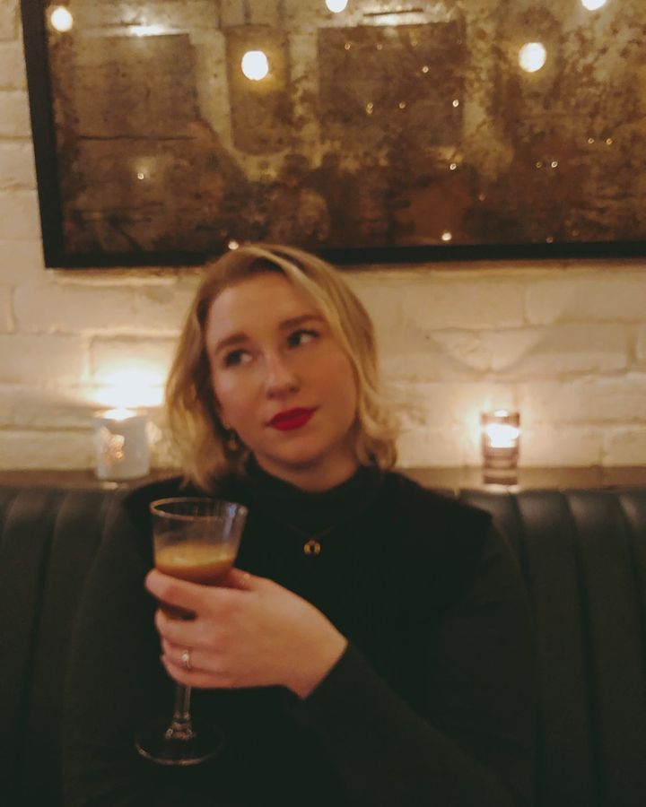 A slightly blurry photo of Juliana in a black vest holding a drink in a restaurant.